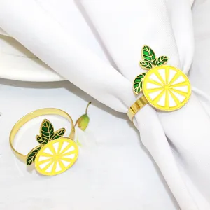 Gold metal lemon napkin ring with enamel yellow slice and green leaves for table decor detail.