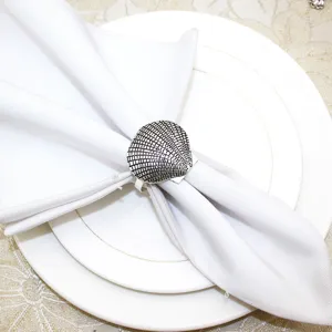 Detailed view of silver seashell napkin ring on white cloth and plate for dining decor.