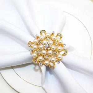Closeup of elegant gold alloy napkin ring decorated with faux pearls and rhinestones on white napkin.