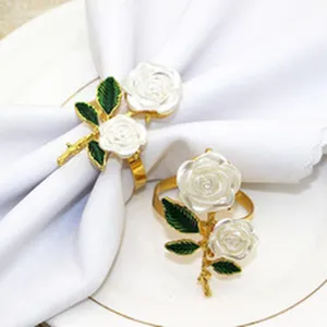 Detailed close-up of elegant gold alloy napkin rings featuring white rose and green leaf design.