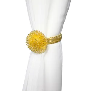 Close-up of gold metal wire curtain tieback featuring an elegant spring ball design for home decor.