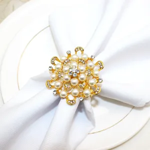 Detail shot of a gold flower napkin ring with pearls and rhinestones on a white napkin.