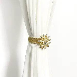 Gold metal curtain tieback detail with faux pearls and rhinestones on white sheer fabric.