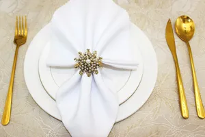 Elegant gold snowflake napkin ring with pearl details for Christmas dinner table decor.