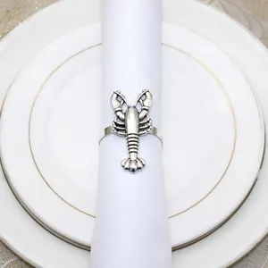 Detailed shot of a vintage silver lobster napkin ring on white fabric and dinnerware plates.