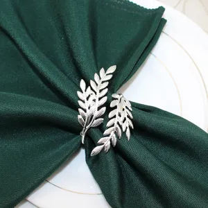 Close-up view of a silver leaf napkin ring beautifully displayed on a green dinner napkin.