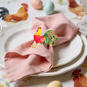 Close up detail of a festive rooster napkin ring holding a pink napkin on a white plate.