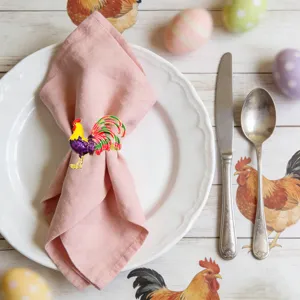 Detailed view of a cute metal rooster napkin ring on a pink napkin for Easter party.