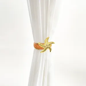 Nahaufnahme eines goldenen Seestern Metall Feder Vorhangraffhalters mit transparenten Vorhängen.