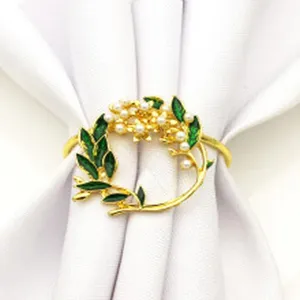 Dettaglio anello per tovagliolo in lega dorata con fiori di perle e foglie verdi per la tavola.