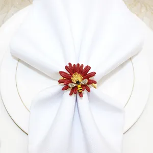 Primo piano di un portatovagliolo con fiore rosso e ape di cristallo su un piatto bianco.