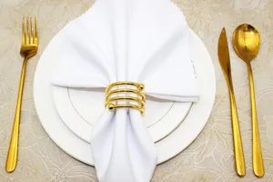 Gold metal spring napkin ring detail view on white cloth napkin and plate table setting setup.