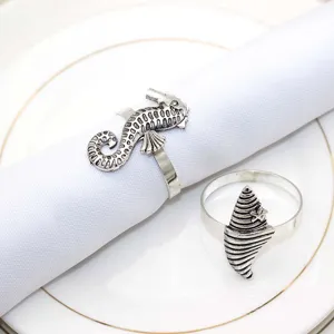 Close-up detail of vintage silver metal seahorse and shell napkin rings on white napkin.