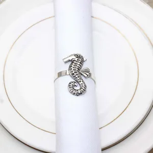 Close up detail view of the metallic silver seahorse napkin ring on white fabric and plate.