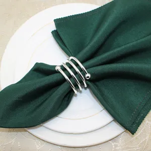 Detail view of a silver metal spring napkin ring holding a green napkin on a white plate.