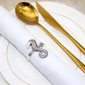 Close-up of a silver metal seahorse napkin ring on white cloth and plate for table decor.