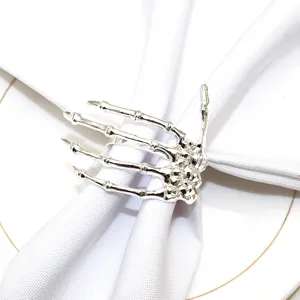 Close up view of silver skeleton hand napkin ring on white cloth, detail shot for Halloween party decor.