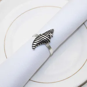 Close-up detail of vintage silver metal seashell napkin ring on clean white cloth and plate.