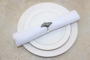Detailed close-up view of vintage metal shell napkin ring with white cloth napkin on plates.