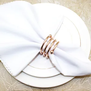 Detail shot of a elegant rose gold spring napkin ring holding white fabric napkin on plate.