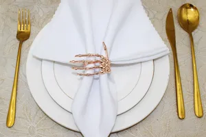 Gold skeleton hand napkin ring detail on white napkin and plate for Halloween party decor.
