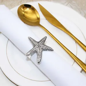 Close-up of a vintage silver starfish napkin ring on a clean white napkin with gold cutlery.