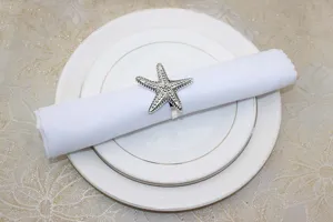 Detail view of a silver starfish napkin ring holding a clean white napkin on fine plates.