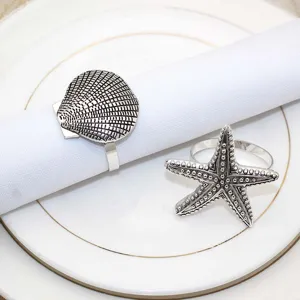 Detail shot of vintage silver metal napkin rings featuring seashell and starfish coastal designs.