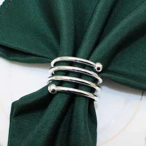 Silver metal spiral napkin ring with double beads holding dark green cloth napkin for table decor