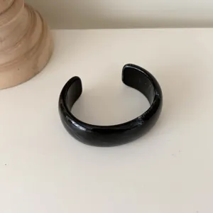 Nahaufnahme des schwarzen Harz breiten offenen Armreifs, glatte Oberfläche minimalistisch.