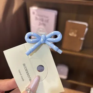 Close-up detail of a cute blue polka dot bow hair clip displayed on a branded card.