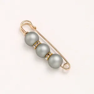 Detail shot of a gold-tone safety pin brooch featuring three grey pearls and sparkling rhinestone spacers.