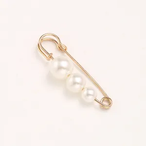 Close-up detail of a gold safety pin brooch decorated with three graded white pearls.