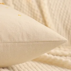 Close-up detail of beige canvas pillow cover with delicate gold star embroidery texture.
