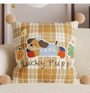 Decorative throw pillow with cute cartoon dog print, plaid pattern and pom-pom corners for sofa.