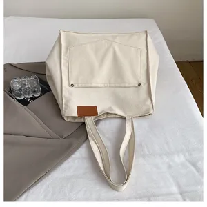 Minimalist canvas tote bag detail, casual off-white shoulder bag with front pocket & patch.