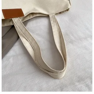 Canvas tote bag detail close-up showing texture, strap handle and decorative leather patch.