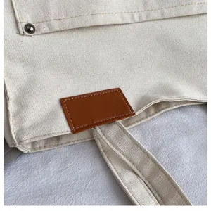 Canvas tote bag detail shot showing leather patch and durable stitching, off-white.