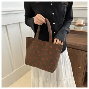 Detailopname van de bruine ribfluwelen tas met een schattig rood aardbeienprintmotief.
