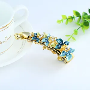 Elegant gold-plated floral banana hair clip with blue enamel and sparkling rhinestones.