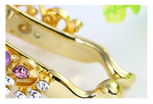 Close-up detail of golden alloy hair clip adorned with sparkling purple and white rhinestones.