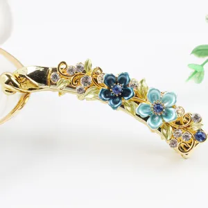 Close-up detail of a gold metal banana hair clip decorated with blue enamel flowers and rhinestones.