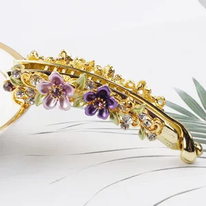 Gold-tone metal banana clip detailed with purple enamel flowers and sparkling rhinestones.