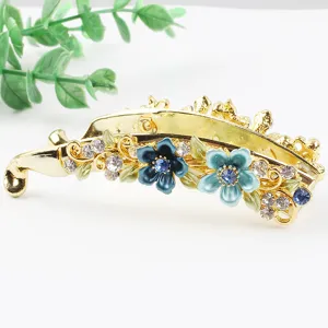 Close-up of a gold metal banana hair clip with blue enameled flowers and clear rhinestones.
