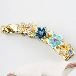 Close-up of golden alloy banana hair clip featuring blue enamel flowers and sparkling rhinestones.