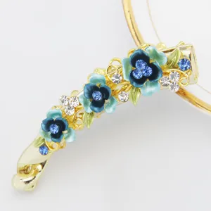 Gold tone alloy banana hair clip featuring blue enamel flowers and sparkling rhinestones for women.