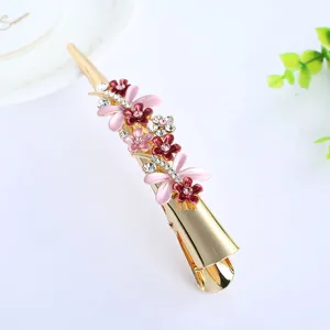 Detail view of golden metal hair clip adorned with enamel flowers and clear stones.