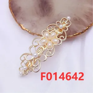 Detailed close-up of a gold metal flower hair clip decorated with white pearls on a cloth backdrop.