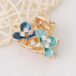 Mini pince à cheveux dorée avec des fleurs émaillées bleues et strass brillants.
