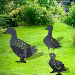 Detail view of black acrylic duck family garden stakes placed on a green lawn for yard art decor.